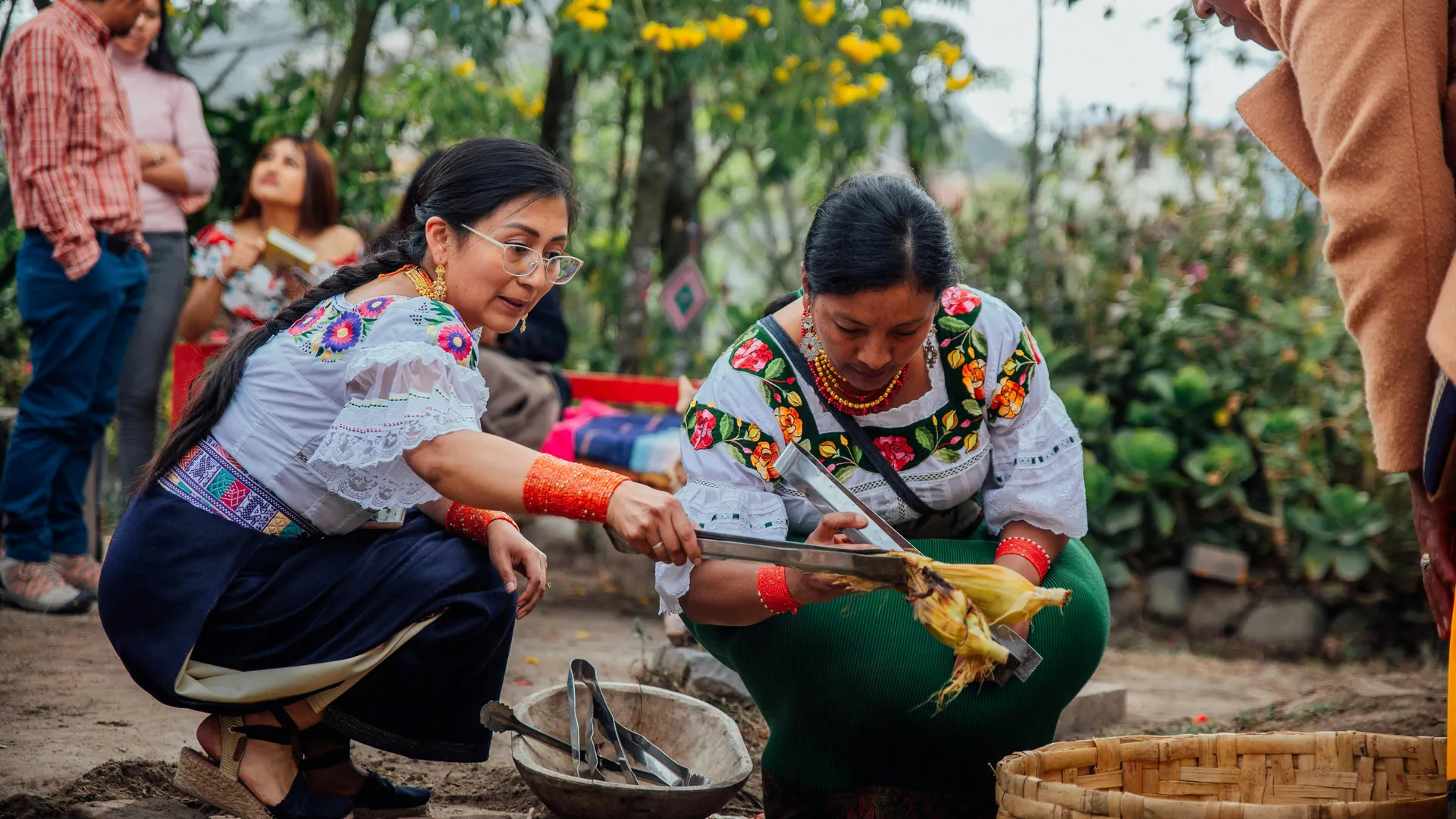 Indigenous women in traditional clothing cook outdoors in Otavalo, Ecuador.